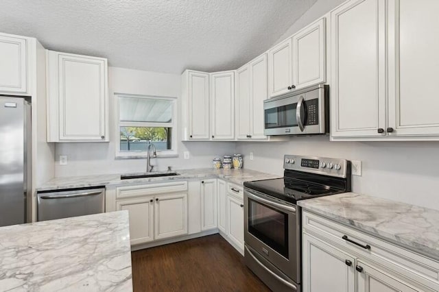 kitchen with dark hardwood / wood-style floors, sink, white cabinets, light stone counters, and stainless steel appliances