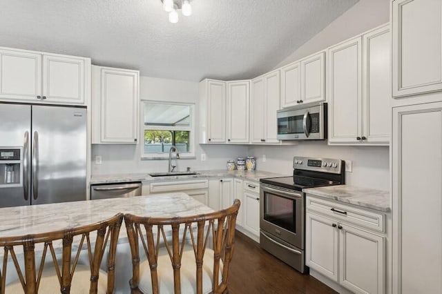 kitchen with sink, a breakfast bar area, white cabinetry, stainless steel appliances, and light stone countertops