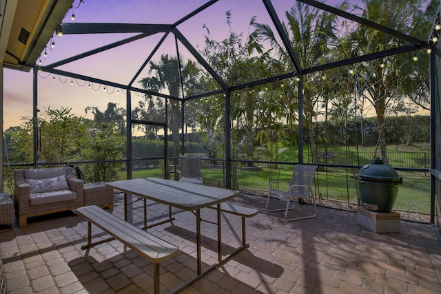 patio terrace at dusk with area for grilling, an outdoor living space, and glass enclosure