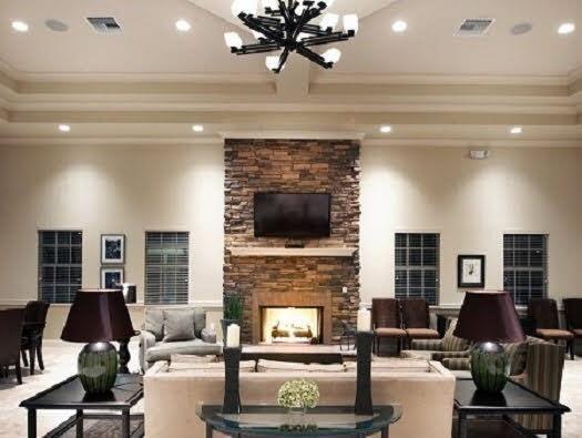 community lobby featuring an inviting chandelier, ornamental molding, and a stone fireplace