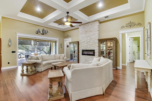 living room with coffered ceiling, a stone fireplace, hardwood / wood-style floors, and a high ceiling