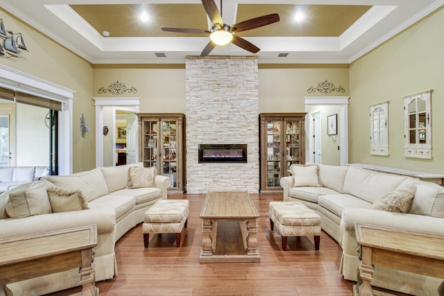 living room with a towering ceiling, hardwood / wood-style floors, a fireplace, a raised ceiling, and crown molding