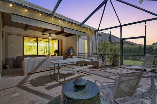 patio terrace at dusk featuring outdoor lounge area, ceiling fan, and a lanai