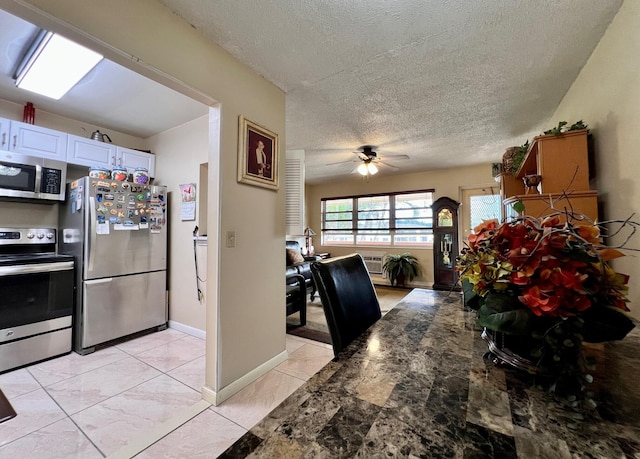 kitchen featuring appliances with stainless steel finishes, dark stone countertops, white cabinets, ceiling fan, and a textured ceiling