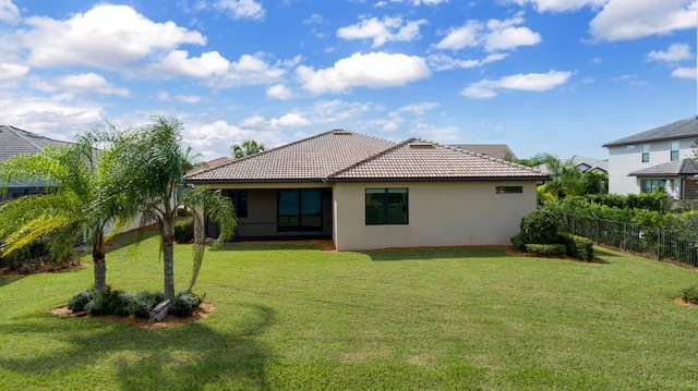 rear view of property featuring stucco siding, a tile roof, fence, and a yard