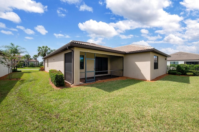 back of property with a lawn, a tile roof, a sunroom, and stucco siding