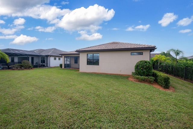 rear view of property with a tiled roof, fence, a lawn, and stucco siding