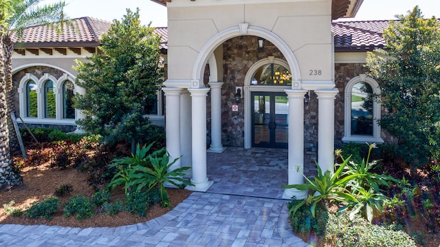 doorway to property with stone siding, french doors, decorative driveway, and stucco siding