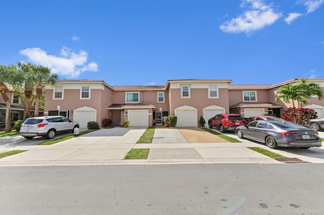 view of property featuring driveway, a tiled roof, an attached garage, and stucco siding