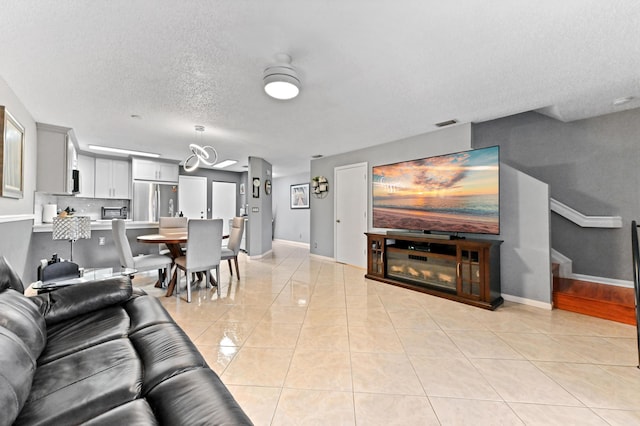 living room with a textured ceiling, light tile patterned flooring, visible vents, and baseboards