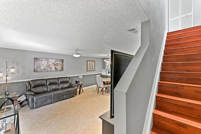 living room featuring light tile patterned floors, a textured ceiling, visible vents, a ceiling fan, and stairway