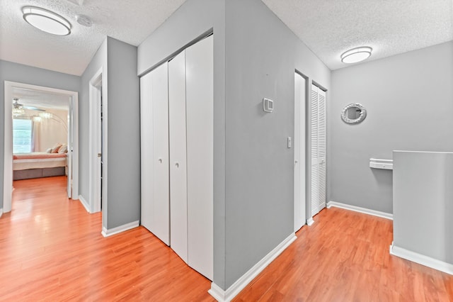 corridor featuring light wood-type flooring, a textured ceiling, and baseboards