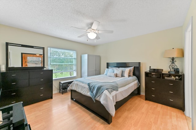 bedroom with light wood-type flooring, ceiling fan, baseboards, and a textured ceiling