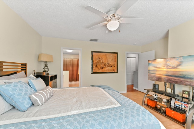 bedroom featuring ceiling fan, a textured ceiling, visible vents, and wood finished floors