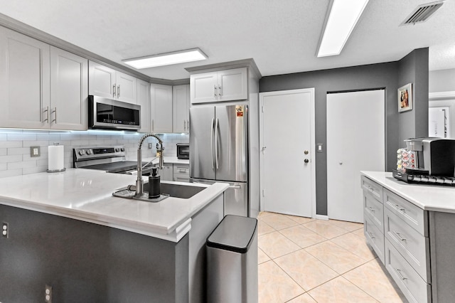 kitchen featuring light tile patterned floors, stainless steel appliances, a peninsula, a sink, and light countertops