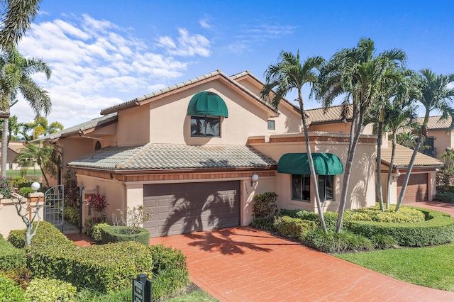 mediterranean / spanish house featuring a tiled roof, decorative driveway, an attached garage, and stucco siding