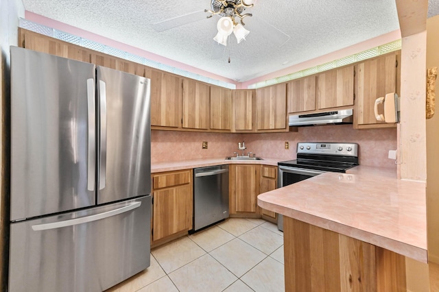 kitchen with sink, appliances with stainless steel finishes, a textured ceiling, light tile patterned flooring, and kitchen peninsula