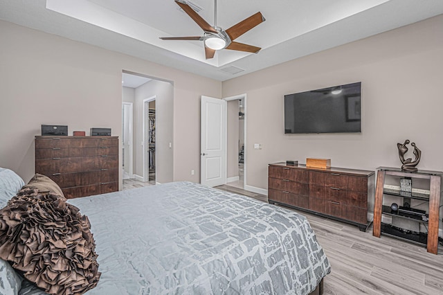 bedroom with a spacious closet, a tray ceiling, ceiling fan, and light hardwood / wood-style flooring