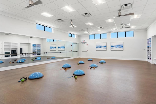 exercise room with a high ceiling, a drop ceiling, and ceiling fan