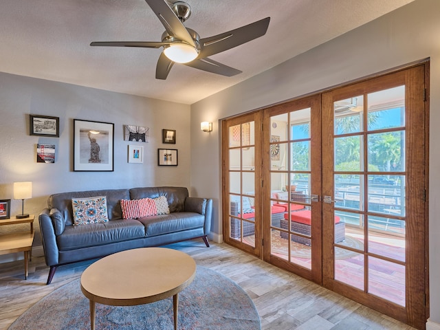 living room with ceiling fan, french doors, a textured ceiling, and light wood-type flooring