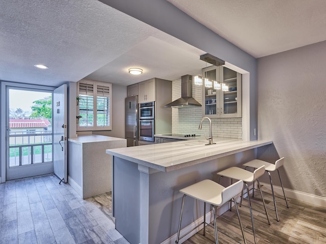 kitchen featuring sink, tasteful backsplash, a kitchen bar, kitchen peninsula, and wall chimney exhaust hood