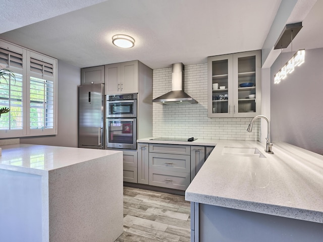 kitchen featuring sink, gray cabinetry, backsplash, stainless steel appliances, and wall chimney range hood