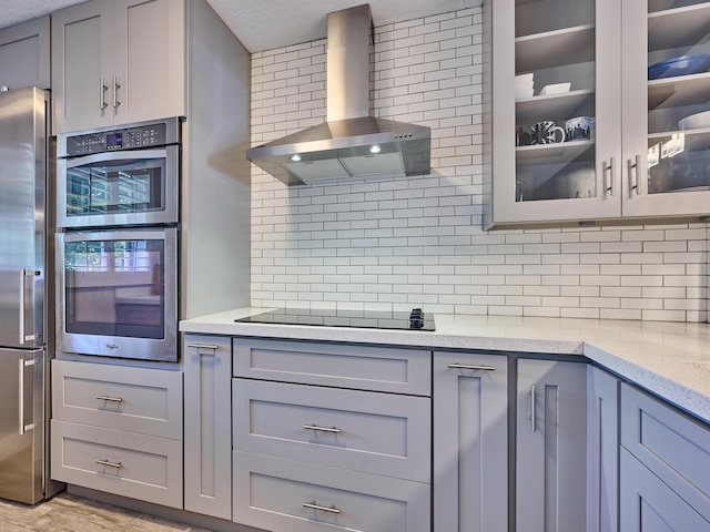 kitchen with appliances with stainless steel finishes, gray cabinets, and wall chimney range hood