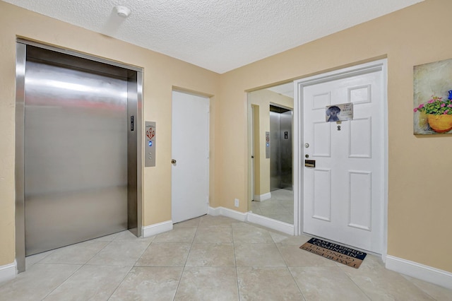 entrance foyer with light tile patterned floors, a textured ceiling, and elevator