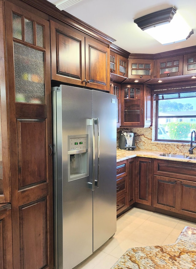 kitchen with light tile patterned flooring, sink, backsplash, light stone counters, and stainless steel fridge with ice dispenser