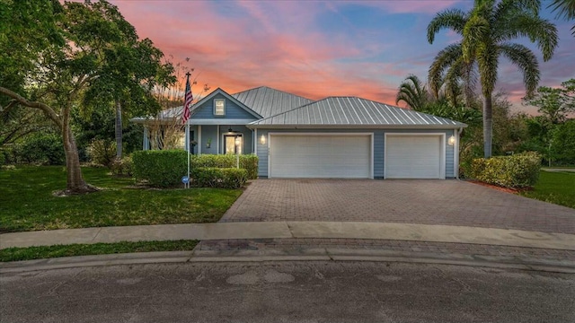 ranch-style home featuring a garage, metal roof, decorative driveway, and a front yard