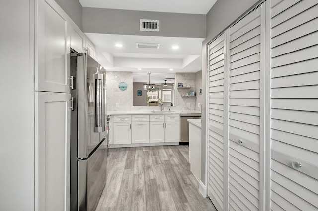 kitchen with sink, light hardwood / wood-style flooring, appliances with stainless steel finishes, white cabinetry, and a raised ceiling