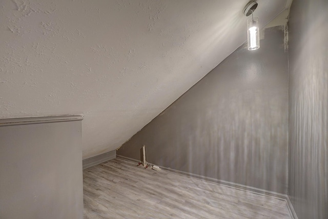 additional living space featuring vaulted ceiling, light hardwood / wood-style flooring, and a textured ceiling