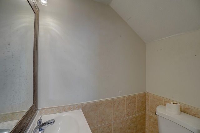 bathroom with toilet, vaulted ceiling, and tile walls