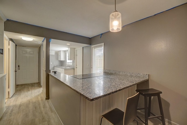 kitchen featuring a breakfast bar area, kitchen peninsula, stone counters, pendant lighting, and black electric stovetop