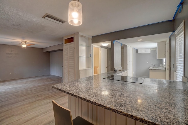 kitchen featuring light hardwood / wood-style flooring, ceiling fan, black electric stovetop, a textured ceiling, and decorative light fixtures