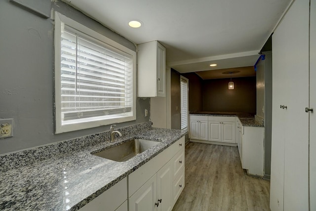 kitchen with stone counters, decorative light fixtures, white cabinetry, sink, and light hardwood / wood-style flooring