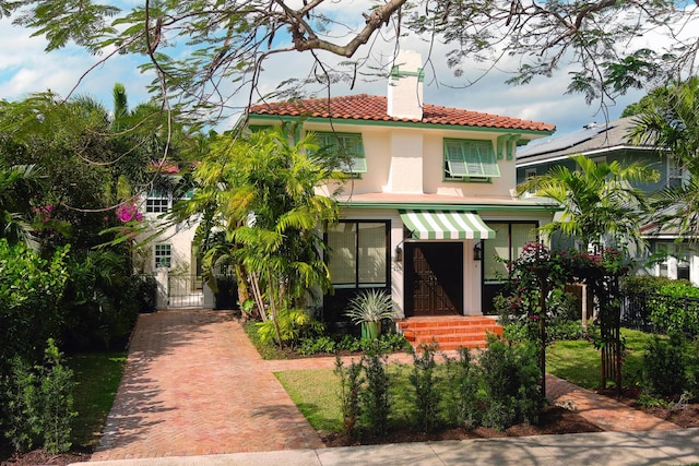 mediterranean / spanish home with a tile roof, a gate, a chimney, and stucco siding