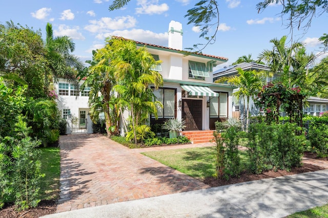 mediterranean / spanish house featuring a gate, a chimney, decorative driveway, and stucco siding