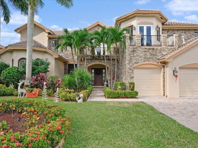 mediterranean / spanish-style home with a garage, a balcony, stone siding, decorative driveway, and stucco siding