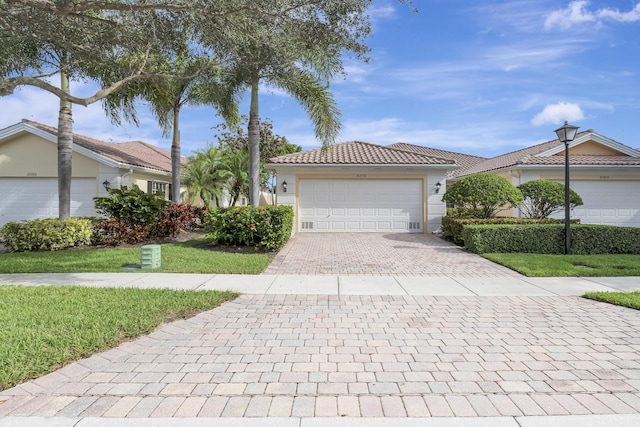 view of front of house with a tile roof, an attached garage, decorative driveway, a front yard, and stucco siding