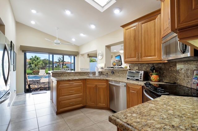 kitchen featuring sink, kitchen peninsula, ceiling fan, stainless steel appliances, and light stone countertops