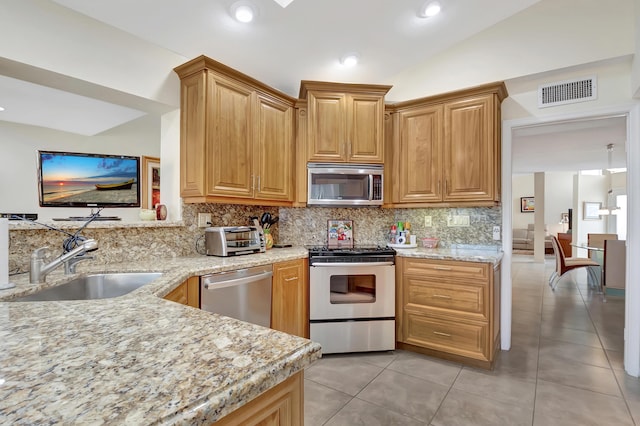 kitchen with lofted ceiling, sink, stainless steel appliances, tasteful backsplash, and light stone countertops