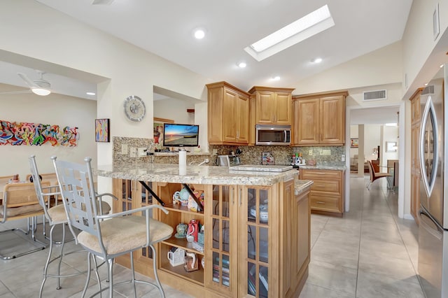 kitchen with lofted ceiling with skylight, appliances with stainless steel finishes, backsplash, light stone counters, and kitchen peninsula