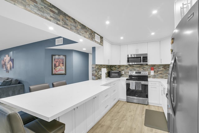 kitchen with a breakfast bar, appliances with stainless steel finishes, white cabinets, decorative backsplash, and kitchen peninsula