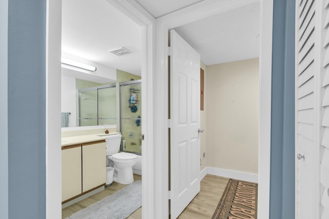 bathroom featuring baseboards, toilet, enclosed tub / shower combo, wood finished floors, and vanity