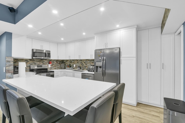 kitchen with stainless steel appliances, a breakfast bar, a peninsula, a sink, and light countertops