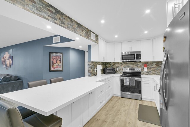 kitchen with stainless steel appliances, a peninsula, visible vents, white cabinetry, and tasteful backsplash