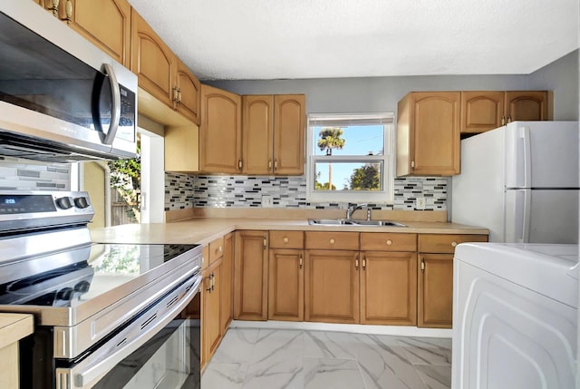 kitchen with appliances with stainless steel finishes, washer / dryer, sink, backsplash, and a textured ceiling