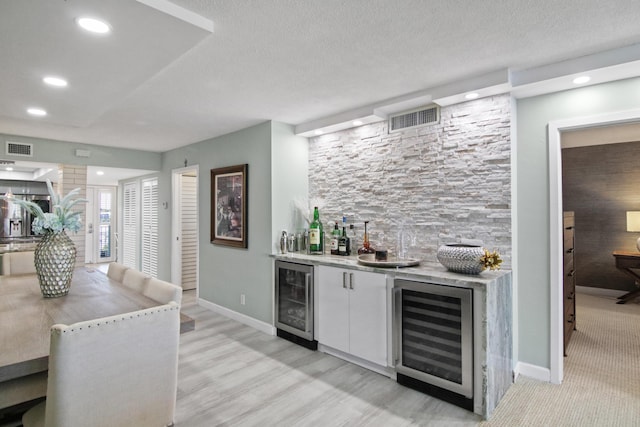 bar with wine cooler, white cabinets, and a textured ceiling