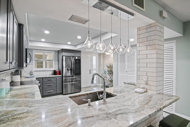 kitchen featuring gray cabinets, pendant lighting, sink, stainless steel fridge, and light stone counters